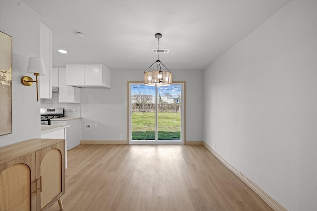 unfurnished dining area featuring light wood-style floors, baseboards, an inviting chandelier, and visible vents