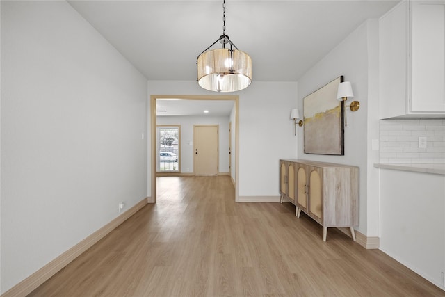 hallway with light wood-style floors, baseboards, and a chandelier