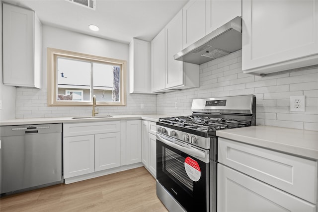 kitchen with a sink, light countertops, white cabinets, under cabinet range hood, and stainless steel appliances