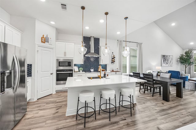 kitchen with wall chimney range hood, light countertops, light wood finished floors, backsplash, and stainless steel appliances