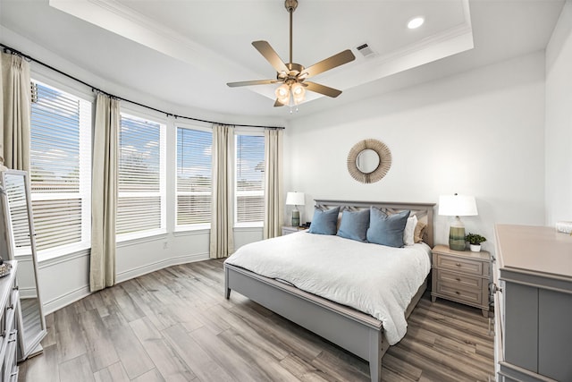 bedroom featuring visible vents, crown molding, wood finished floors, a tray ceiling, and recessed lighting