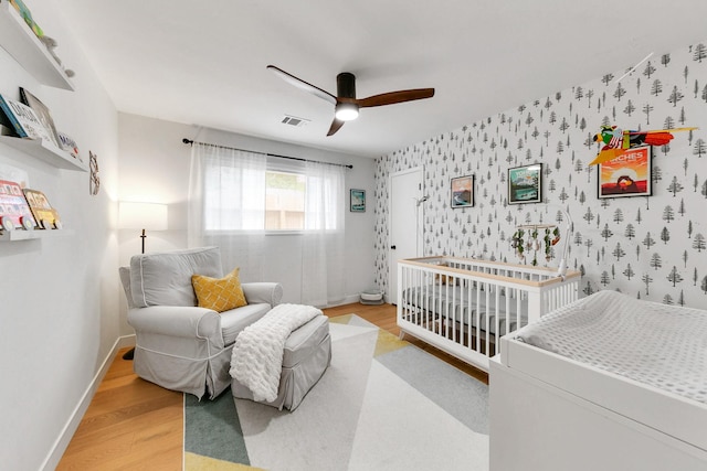 bedroom with a ceiling fan, baseboards, wallpapered walls, wood finished floors, and visible vents