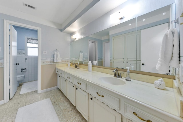 full bathroom with a sink, toilet, double vanity, and visible vents