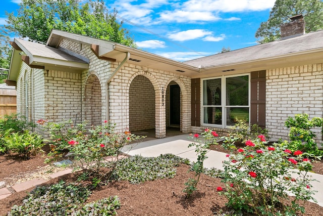 doorway to property featuring a patio, a chimney, and brick siding