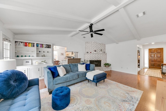 living room featuring ceiling fan, a brick fireplace, light wood-style flooring, vaulted ceiling with beams, and visible vents