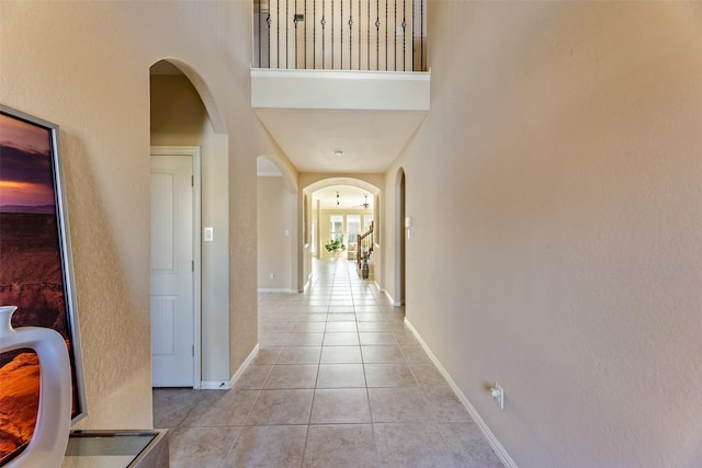corridor featuring light tile patterned floors, arched walkways, baseboards, and a towering ceiling