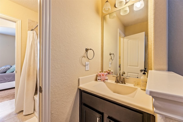 ensuite bathroom with vanity, connected bathroom, a textured wall, and tile patterned flooring