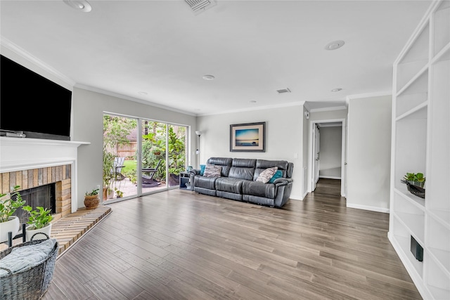 living room featuring a brick fireplace, visible vents, ornamental molding, and wood finished floors
