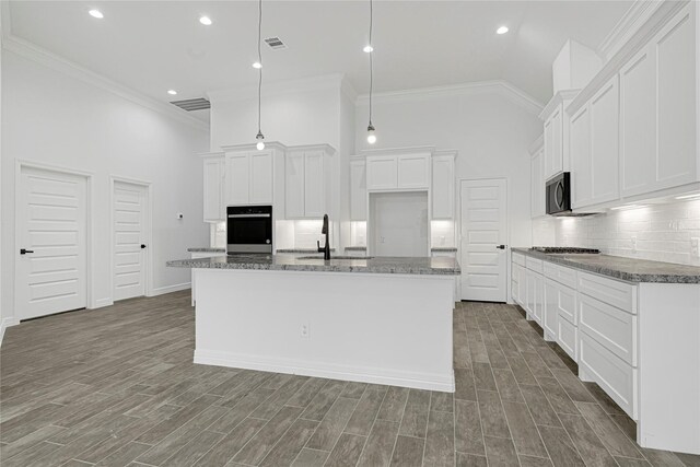 123 Big Spring Dr, Anahuac, TX 77514 - kitchen with stainless steel appliances, high vaulted ceiling, decorative backsplash, an island with sink, and white cabinetry