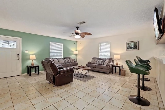 living area with light tile patterned floors, plenty of natural light, ceiling fan, and visible vents