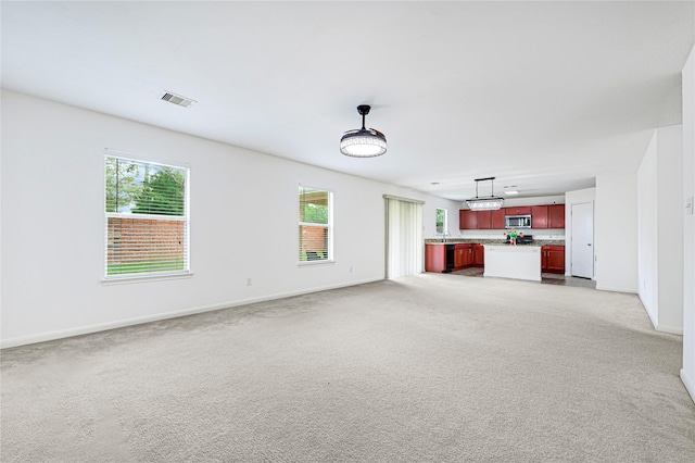 unfurnished living room with light colored carpet, baseboards, visible vents, and a sink