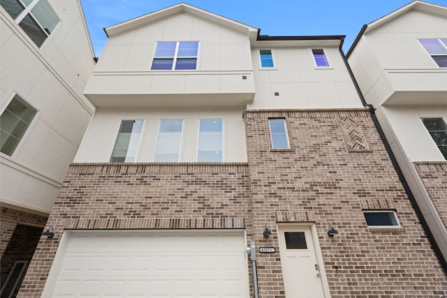 townhome / multi-family property featuring brick siding, a garage, and stucco siding