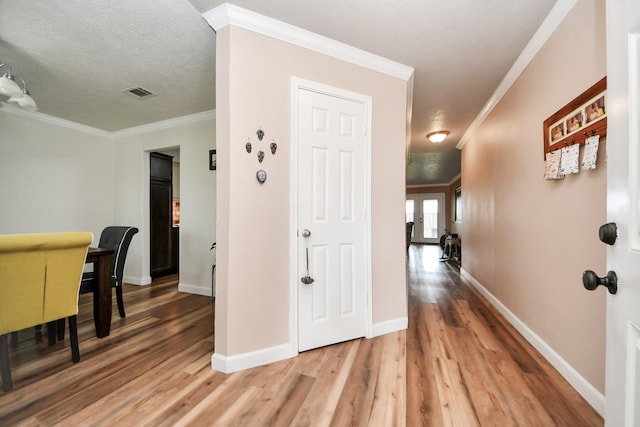 hall with crown molding, baseboards, visible vents, and light wood finished floors