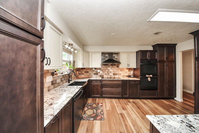 kitchen with tasteful backsplash, a sink, black appliances, light wood finished floors, and wall chimney exhaust hood