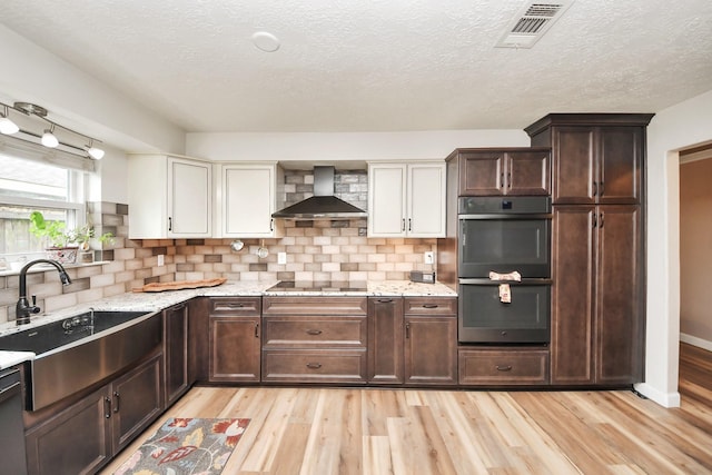 kitchen with visible vents, double oven, wall chimney range hood, a sink, and light wood finished floors