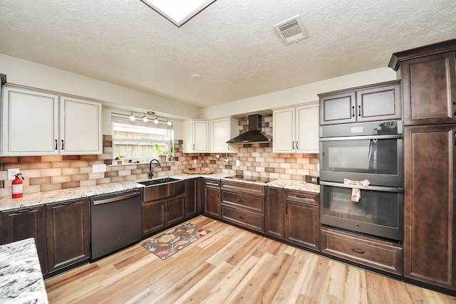 kitchen with dishwashing machine, wall chimney exhaust hood, a sink, light wood-style flooring, and double wall oven