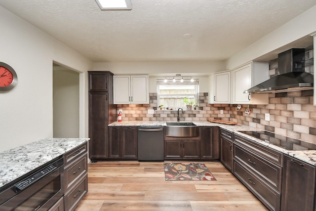 kitchen with black electric stovetop, a sink, dishwasher, built in microwave, and wall chimney exhaust hood
