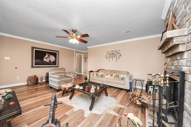 living area featuring a ceiling fan, visible vents, a brick fireplace, wood finished floors, and baseboards