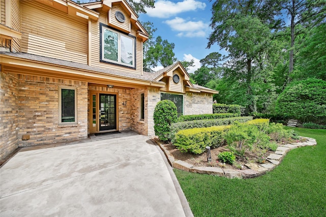 view of exterior entry with brick siding, a patio area, and a yard