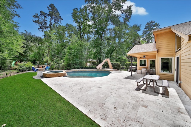 view of pool featuring ceiling fan, a lawn, a pool with connected hot tub, a patio, and a water slide