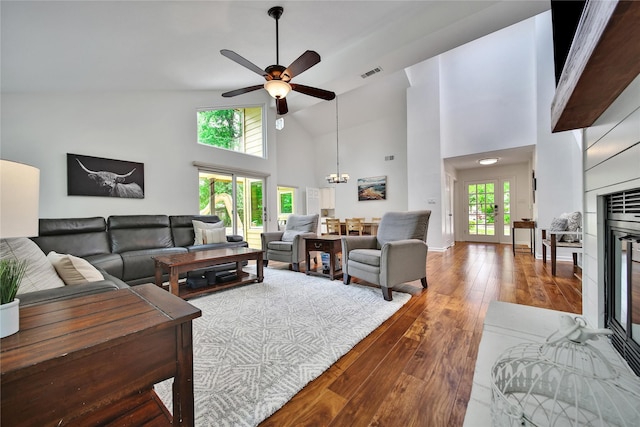 living area with visible vents, baseboards, high vaulted ceiling, hardwood / wood-style flooring, and ceiling fan with notable chandelier