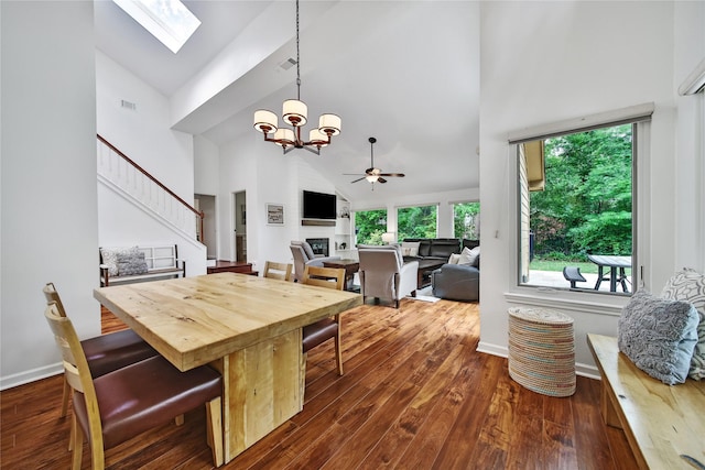 dining room featuring a skylight, high vaulted ceiling, ceiling fan with notable chandelier, and dark wood-type flooring