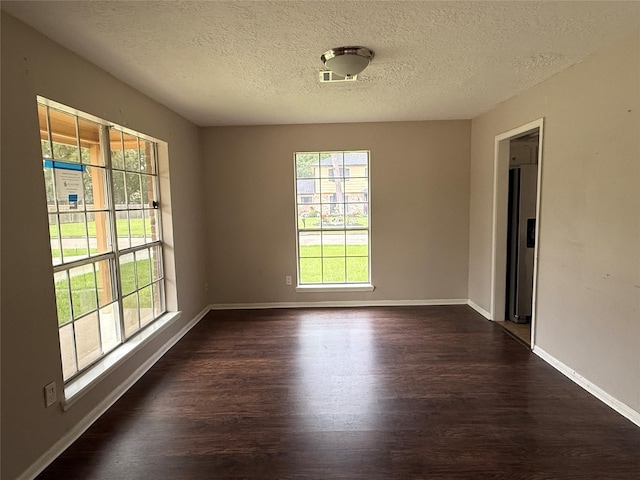 spare room featuring baseboards, dark wood finished floors, a textured ceiling, and a wealth of natural light