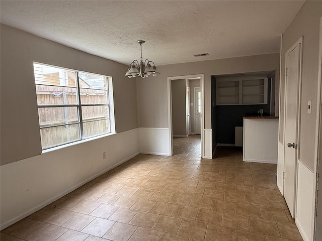unfurnished dining area featuring an inviting chandelier, baseboards, a textured ceiling, and visible vents