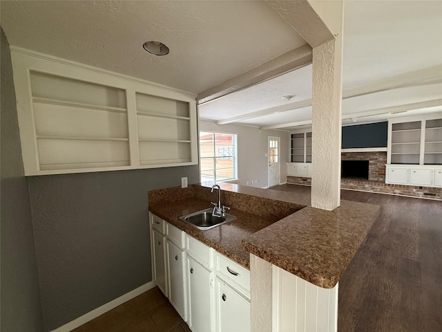 kitchen with built in features, a peninsula, dark countertops, a fireplace, and a sink