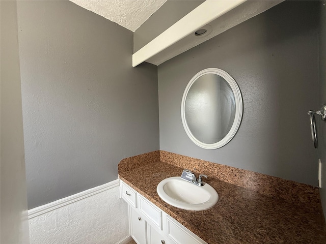 bathroom featuring vanity, a textured ceiling, and wainscoting