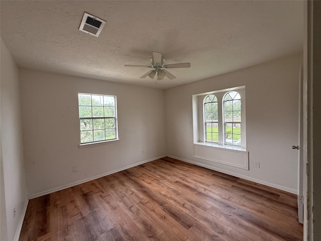 empty room with visible vents, ceiling fan, wood finished floors, and a healthy amount of sunlight