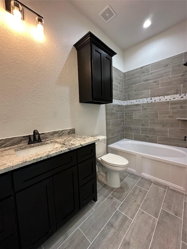 507 Kickapoo Dr, Anahuac, TX 77514 - full bathroom featuring visible vents, wood finish floors, vanity, toilet, and a textured wall