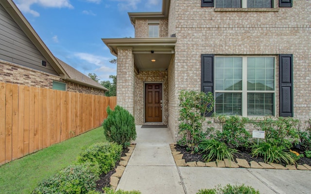 view of exterior entry featuring brick siding and fence