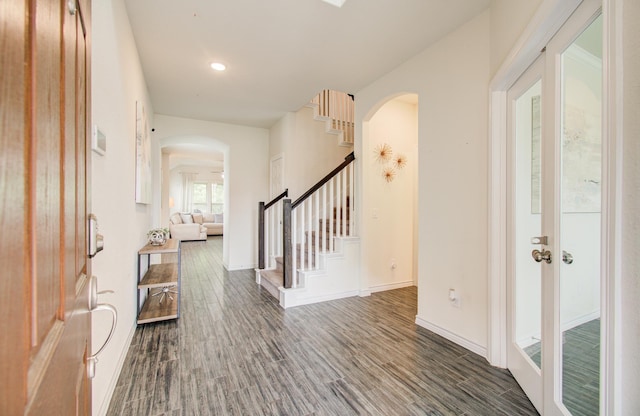 entrance foyer with arched walkways, baseboards, dark wood finished floors, and stairway