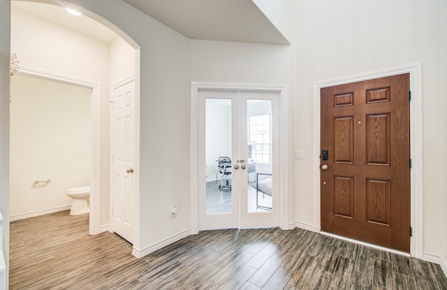 foyer with arched walkways, baseboards, french doors, and wood finished floors
