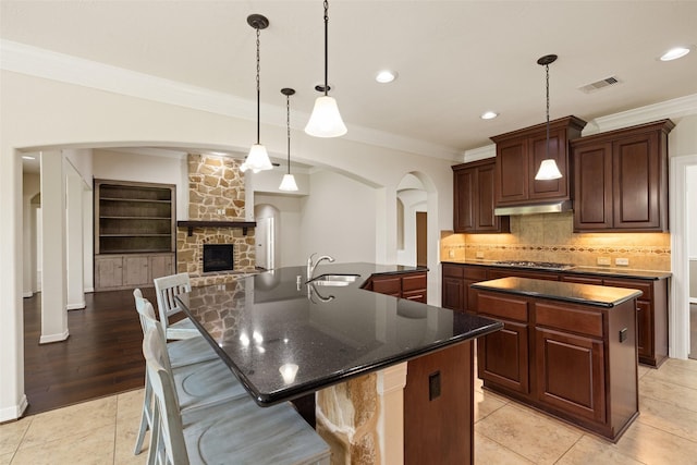 kitchen featuring a large island, visible vents, crown molding, arched walkways, and a fireplace
