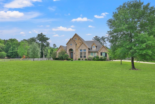 french country style house featuring fence, brick siding, a front lawn, and stone siding