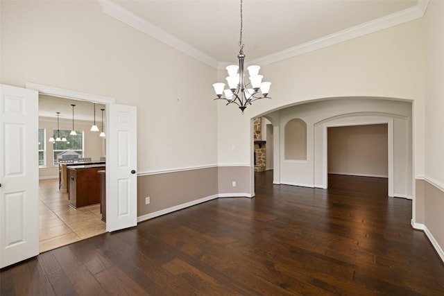 unfurnished dining area with an inviting chandelier, crown molding, baseboards, hardwood / wood-style flooring, and arched walkways