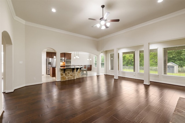 unfurnished living room with arched walkways, ornamental molding, a ceiling fan, and dark wood finished floors