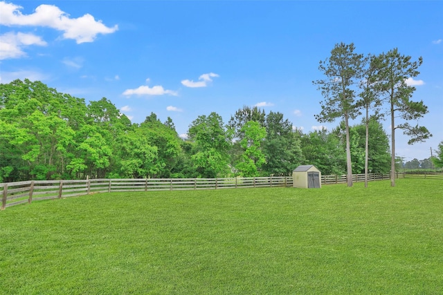 view of yard featuring fence, a storage unit, a rural view, an outdoor structure, and a wooded view