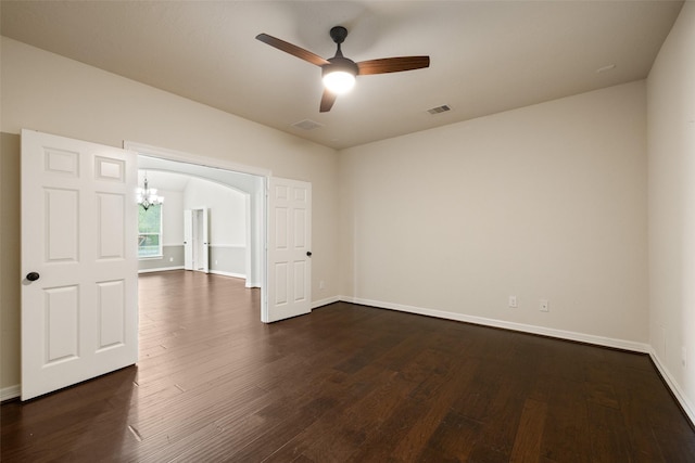 empty room featuring baseboards, dark wood finished floors, ceiling fan with notable chandelier, and visible vents