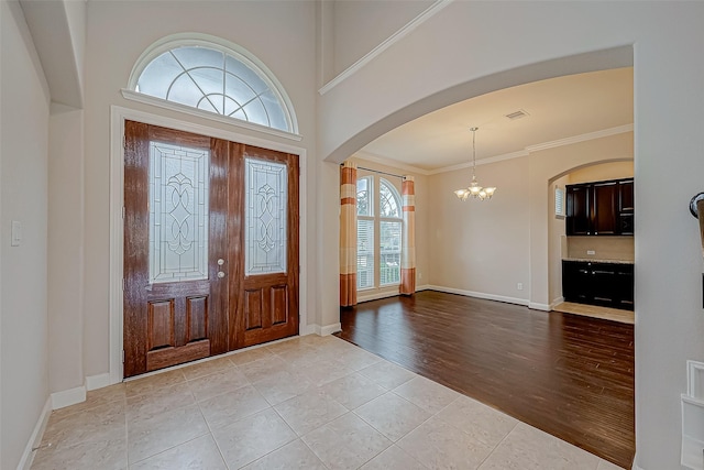 tiled entrance foyer with arched walkways, baseboards, a notable chandelier, and ornamental molding