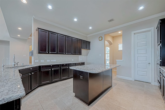 kitchen featuring arched walkways, backsplash, light stone countertops, and ornamental molding