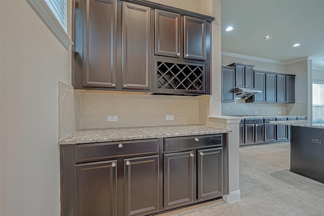 kitchen featuring tasteful backsplash, light stone countertops, ornamental molding, under cabinet range hood, and recessed lighting