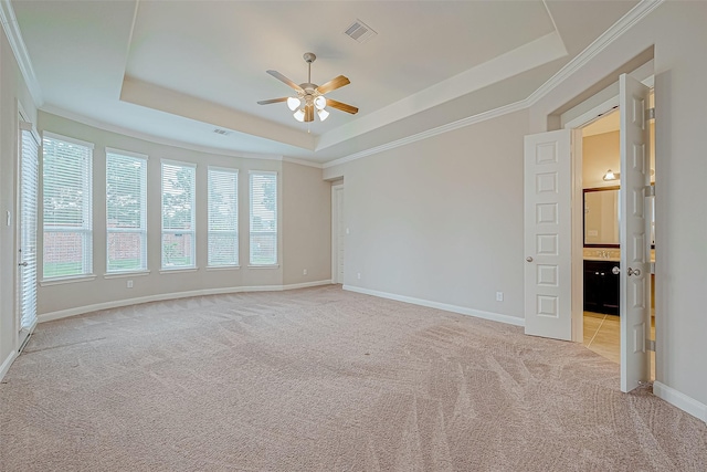 spare room with a ceiling fan, visible vents, a raised ceiling, baseboards, and light carpet
