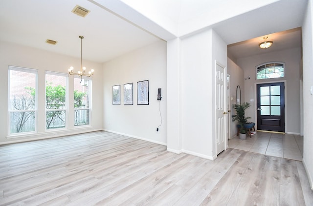 foyer featuring baseboards, a notable chandelier, light wood-style flooring, and visible vents