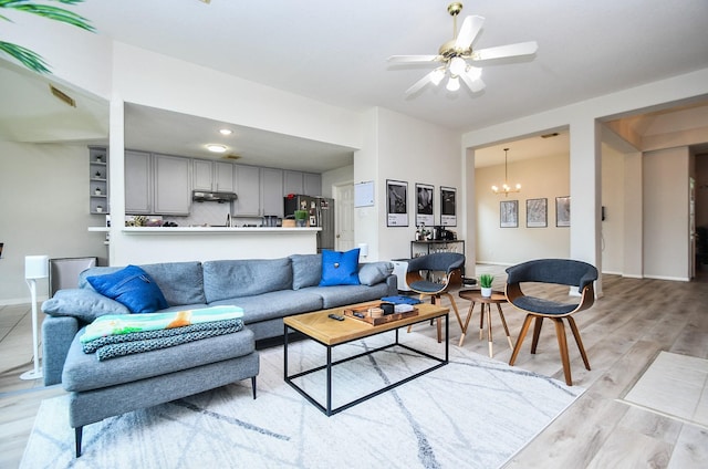 living room with baseboards, ceiling fan with notable chandelier, and light wood-type flooring