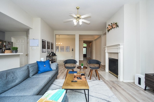 living room featuring light wood-style floors, a high end fireplace, baseboards, and ceiling fan with notable chandelier