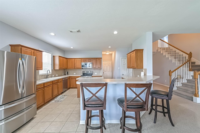 kitchen featuring visible vents, a peninsula, a breakfast bar area, a sink, and stainless steel appliances