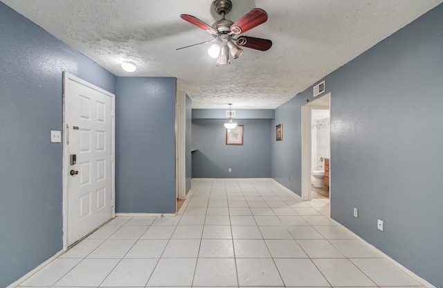 interior space featuring ceiling fan, a textured ceiling, visible vents, light tile patterned floors, and baseboards